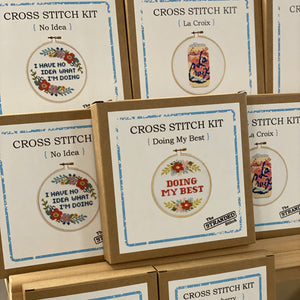 Cross stitch kits with embroidered designs on cardboard boxes.
