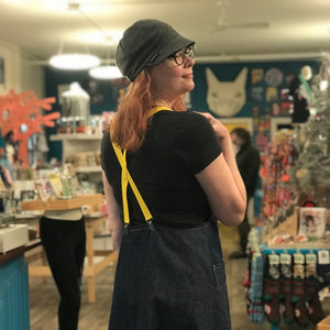 Person wearing a dark denim apron with yellow suspenders in a store setting.