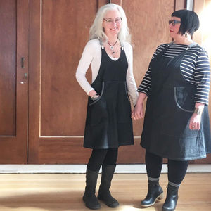 Two women wearing black Shift aprons standing in front of a wooden door.