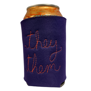 A purple fabric can cooler sleeve with orange embroidered text reading 'they them', shown holding a can on a plain white background.