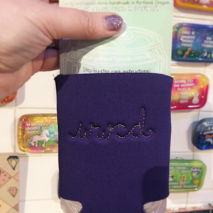 A purple neoprene drink holder that has "wwcd" embroidered on the back.