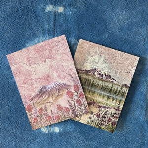Two greeting cards with nature-themed designs on a textured blue surface.