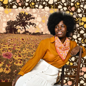 Person modeling a patterned bandana wearing a yellow top and white skirt against a collaged floral background