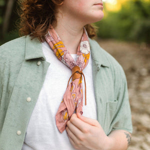 Person wearing a white t-shrit and a green button down modeling a patterned bandana as a scarf.