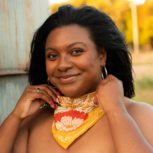A woman modeling a yellow floral patterned bandana, which is tied around her neck as a scarf.
