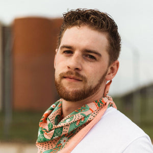 Person wearing a white t-shirt and modeling a pink patterned bandana against a blurred background.