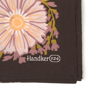 Closeup of a corner of a floral patterned bandana, showing a brown background and a pink flower with peach, white, and mauve details.
