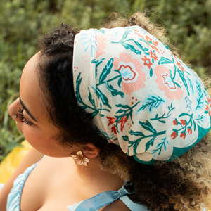 A floral patterned bandana modeled as a headscarf on a woman with curly hair wearing a blue top.