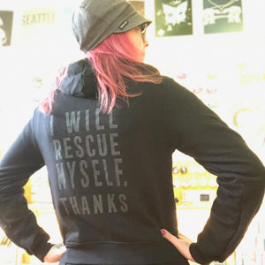 Person wearing a black hoodie with text on the back that says "I will rescue myself, thanks", standing in a casual setting.