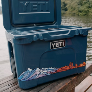 Blue YETI cooler with a scenic design on a wooden dock by a body of water.
