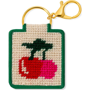 A needlepoint keychain featuring a design of two cherries on a white background with a green border and gold hardware attached.