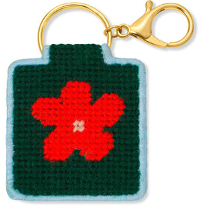 Needlepoint keychain featuring a design of a red flower on a dark green background with a blue background and gold hardware.