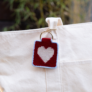Needlepoint keychain with a heart design attached to a white canvas bag.