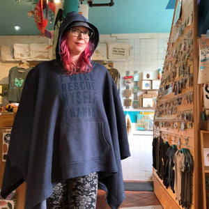 Person wearing a dark blue poncho with text that says "I will rescue myself, thanks" at Ugly Baby's storefront in Seattle, WA.