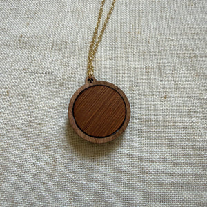 Back view of a wooden pendant necklace on a light fabric background