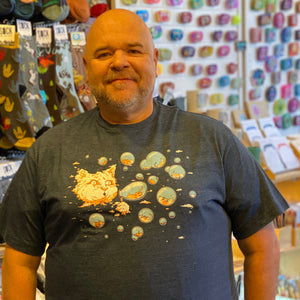 Person wearing a blue t-shirt with cartoon cat designs. There is a large cloud in the sky that looks like a giant cat head. The cat head is blowing bubbles that have tiny kitties inside.