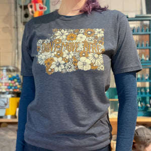 Person wearing a blue t-shirt with floral design and text that says "Don't Move Here" in a store setting. The floral design is in the shape of Washington state.