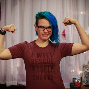Person with blue hair wearing a maroon t-shirt with text that says "I will rescue myself, thanks", flexing muscles indoors.