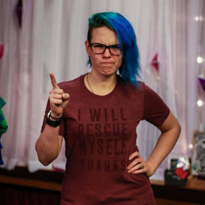 Person with blue hair wearing a maroon t-shirt with text that says "I will rescue myself, thanks", pointing at the camera.