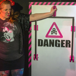 Person posing with a 'DANGER' sign at an event while wearing an astronaut unicorn shirt.
