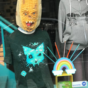 Person wearing a zombie corn head mask and a shirt with an island that is in the shape of a cat.