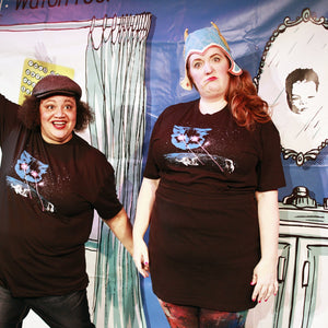 Two people wearing matching black t-shirts with a graphic design in front of a colorful backdrop.