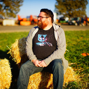 A person sitting on a bale of hay, wearing a gray hoodie and a black tshirt with a cat head shooting lasers out of his eyes.