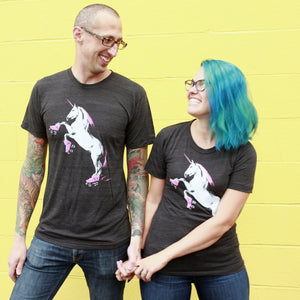 Two people wearing black t-shirts with unicorn graphics against a yellow wall.