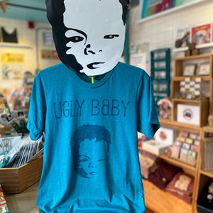 Heather teal t-shirt with 'Ugly Baby' design in a store setting.