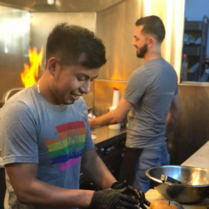 Two men preparing food in a kitchen with flames in the background