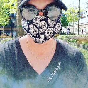 Person wearing a black face mask with white patterns outdoors. They are wearing a shirt that says "no, thank you" around the neckline in cursive.