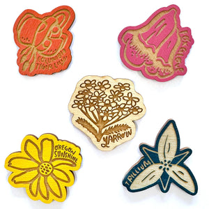 Set of five wooden magnets with floral designs and text on a white background