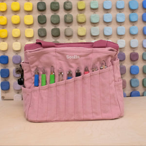 Pink tool bag with colorful tools against a multicolored square patterned wall.