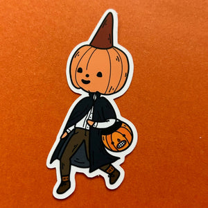 A die-cut sticker featuring a cute cartoon pumpkin character dressed as a vampire, holding a small jack-o'-lantern bucket, shown on a textured orange background.