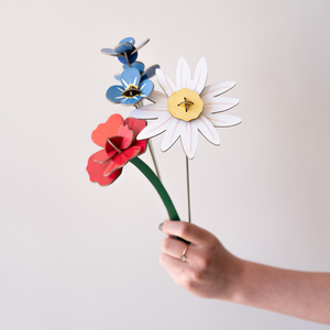 A hand holding a bouquet of cardboard flowers, including a daisy, rose, and foreget-me-nots