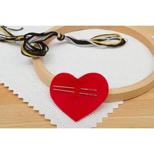 Example of cross stitch kit contents, including fabric, hoop, thread, and two needles in a red heart-shaped piece of felt.