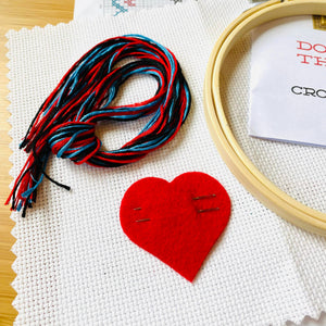 Embroidery hoop, red heart, and colorful thread on a wooden surface