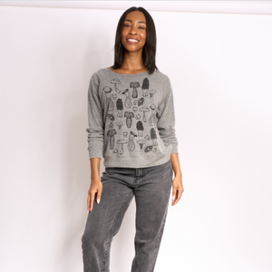 Person wearing a gray sweater with a mushroom pattern and gray jeans against a white background.