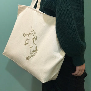 A cream colored tote bag with a roller skating unicorn printed in gold ink.