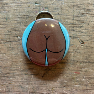 Bottle opener keychain featuring a design of a brown butt on a blue background on top of a wooden surface.
