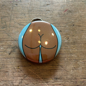 Bottle opener keychain featuring a design of a brown butt with a blue background on top of a wooden surface.