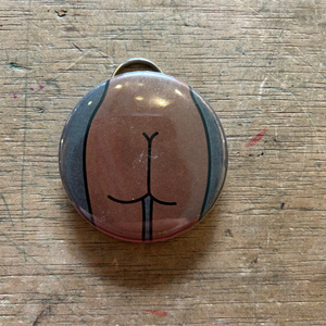 Bottle opener keychain featuring a design of a brown butt with a gray background on top of a wooden surface.