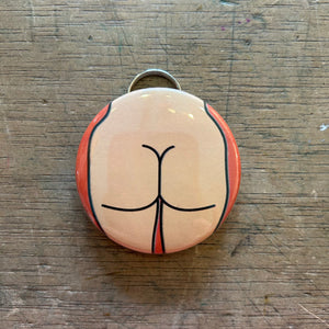 Bottle opener keychain featuring a design of a light colored butt on an orange background on top of a wooden surface.