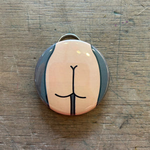A bottle opener keychain featuring a light colored butt with a gray background on top of a wooden surface.