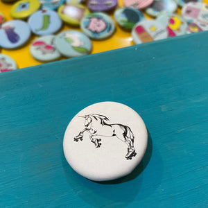 Round button with unicorn design on a blue surface, with colorful buttons in the background.