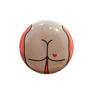 Round magnet with a cartoon butt illustration against a white background