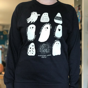 Black sweatshirt with white ghost illustrations worn by a person in a store setting.