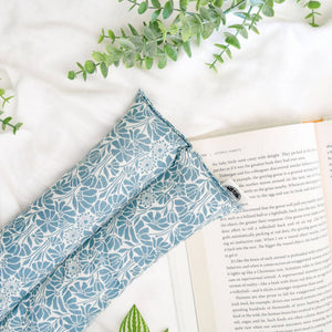 Blue floral hot/cold pack on a white surface with an open book and green leaves.