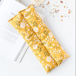 Yellow floral-patterned hot/cold pack on a white surface with a book