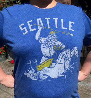 Blue unisex crew t-shirt by Factory 43. It says Seattle and has a mariner wearing a baseball hat and glove and being pulled by two horse mermaids. 